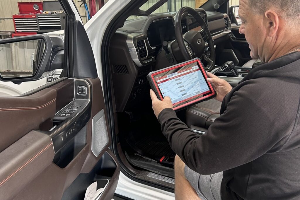 A technician sits beside the driver’s seat of a pickup truck while using a diagnostic tablet to perform ADAS recalibration after a windshield replacement in a Spring, TX auto glass shop.